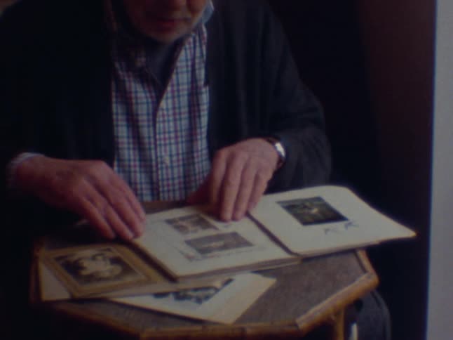 Elderly man sitting at home smiles while flipping through a photo album