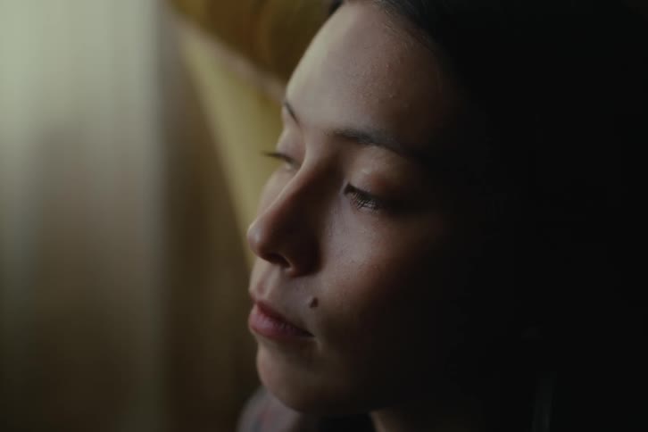 A young woman in a room looks around nervously