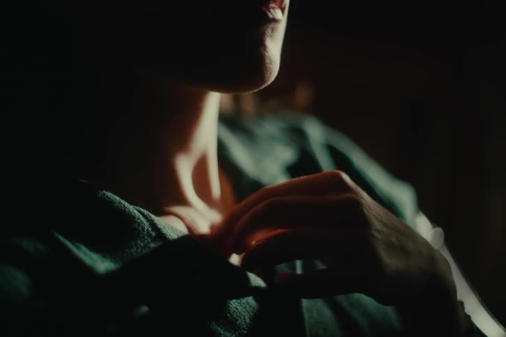 A woman sits in a room and twists her necklace with her fingers