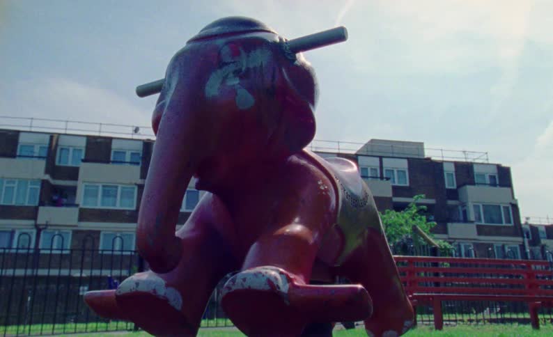 Close up of a red spring elephant rideon toy on a park near to residential buildings