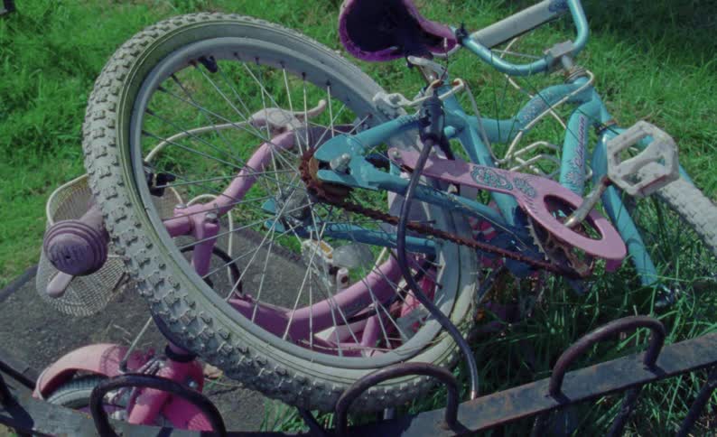 N overturned damaged bicycle lying on grass chained to a bicycle rack