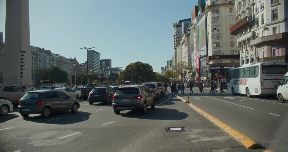 A bustling urban street with cars and buses surrounded by tall buildings under a clear blue sky