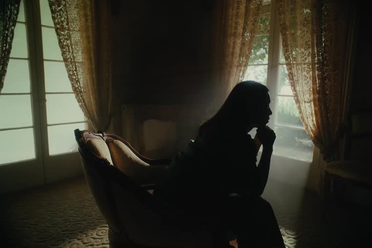 A woman with long hair sits in a chair in a darkened room