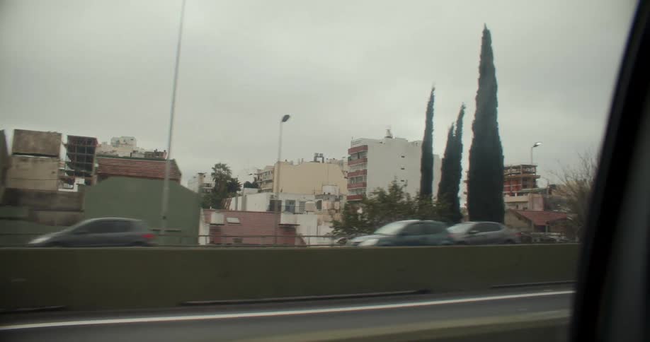 A view of a car interior with a view out the window with several cars passing by and buildings behind