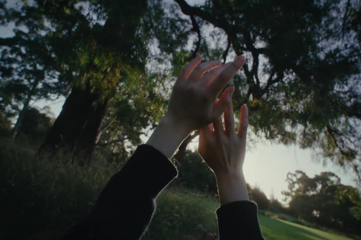 Woman moves her hands together in the air while lying down in a field outdoors on a sunny day