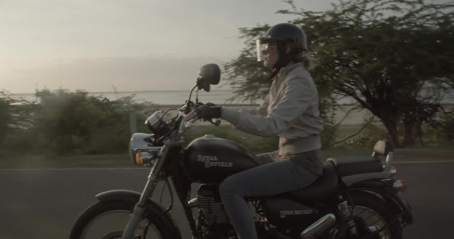 Woman riding her motorcycle on a road next to the sea as the sun is setting