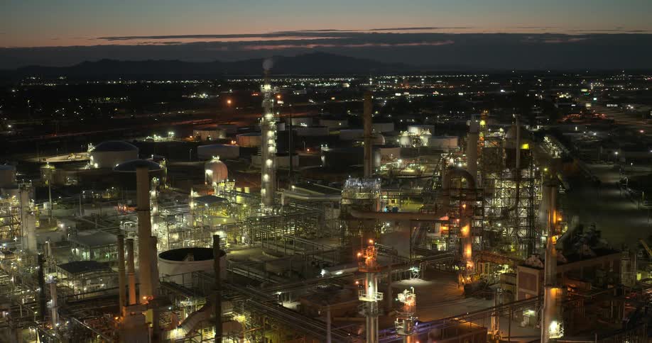 A large refinery on the edge of a city lit up at dusk