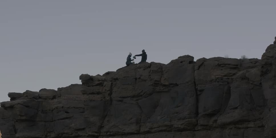 Two people on a high cliff sitting and pouring a beverage