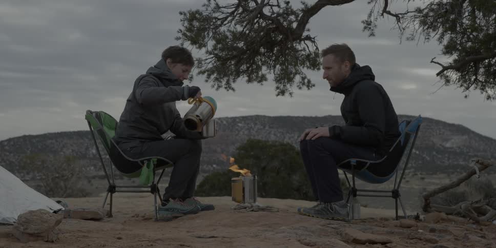 A man at a camp pours a drink for another camper