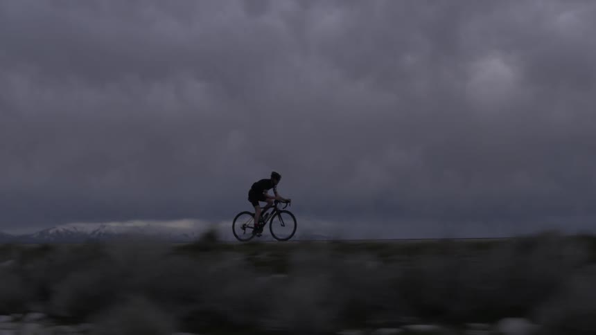 Bicyclist pedaling on a flat road on an extremely cloudy evening