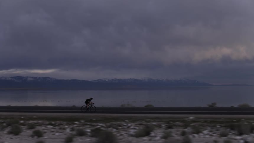 A person rides a bike along a road with dark clouds in the distance