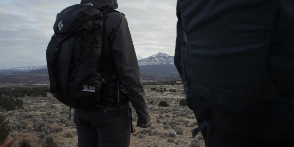 Two people with backpacks standing and observing snowy mountains
