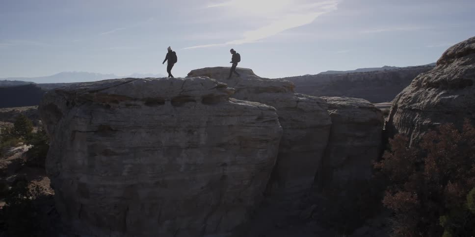 Two people hiking across large rock formations on sunny day
