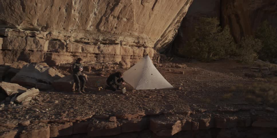 Two people set up a tent in a valley