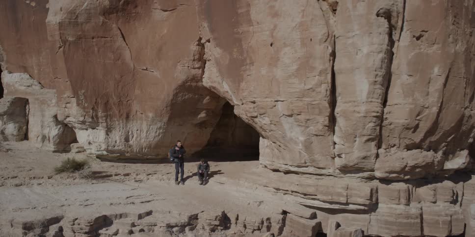 Aerial view of a couple coming out of a cave in a large rock formation and then sitting down
