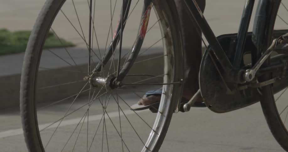 A person wearing flip flops pedals their bicycle down the road