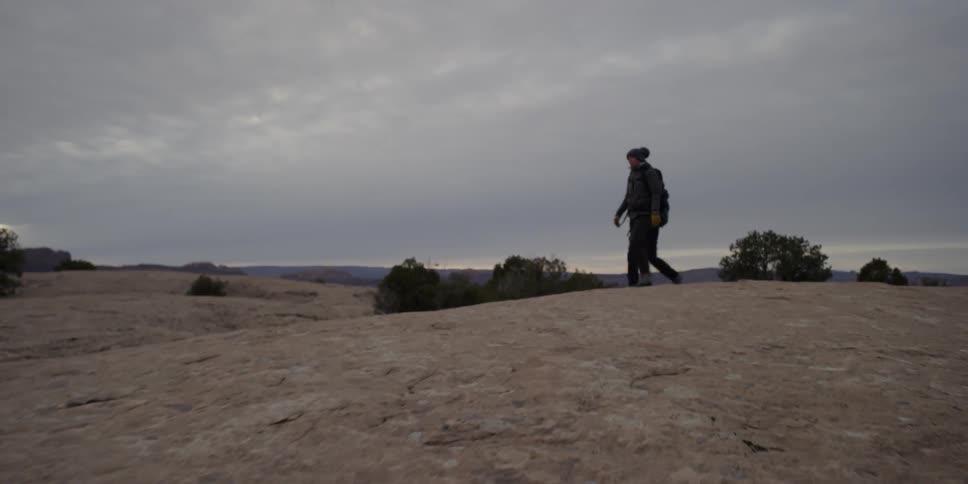 Two people wearing backpacks hiking across large bald rocks