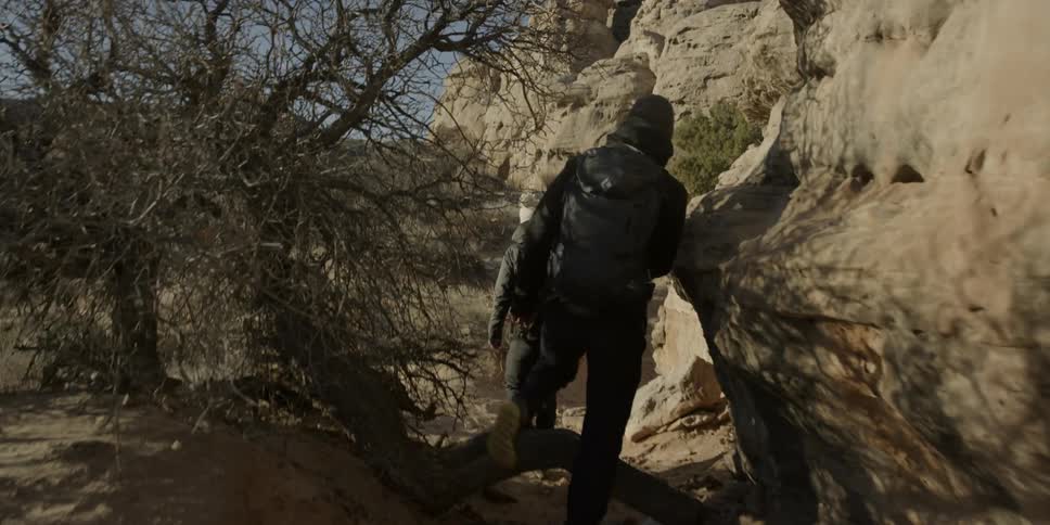 Two hikers following a trail next to a rocky wall