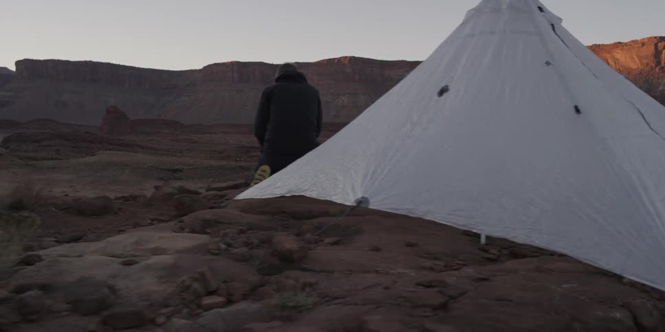 A couple cooks on a campfire outside their tent
