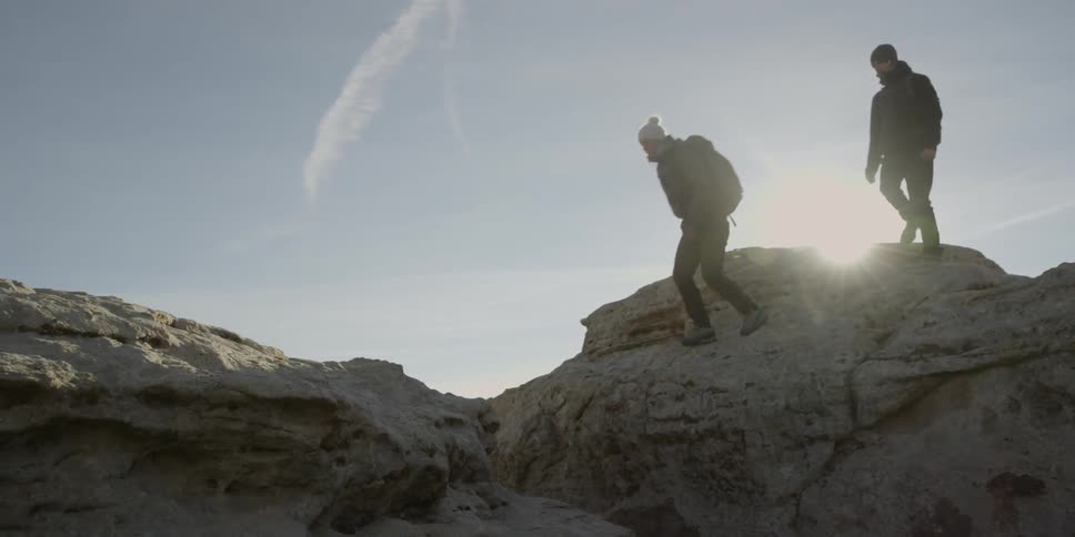 Two people walk on the top of a mountain jumping around