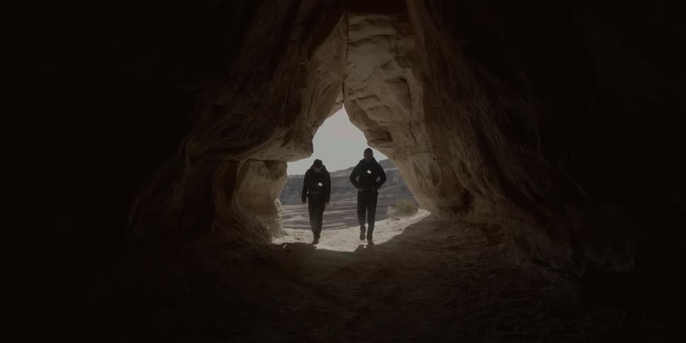 Two people walk into a dark cave