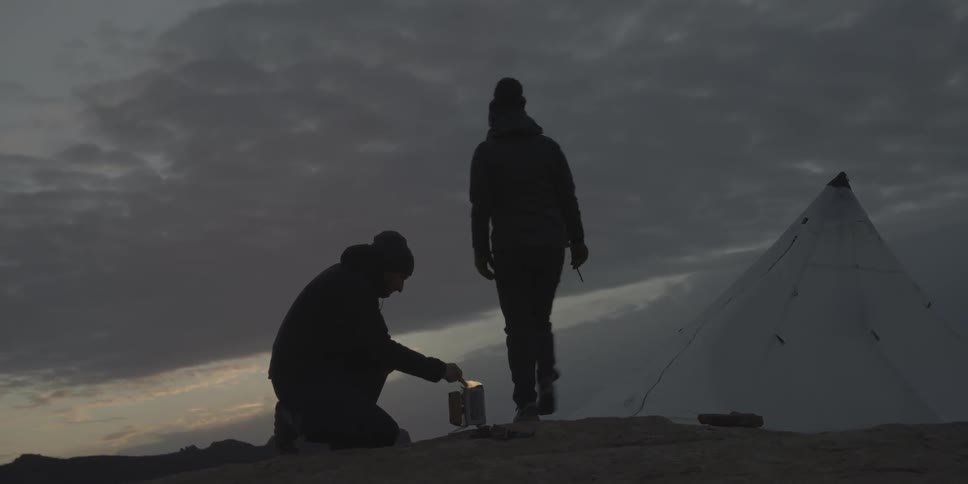 Two people are at a campfire at sunset