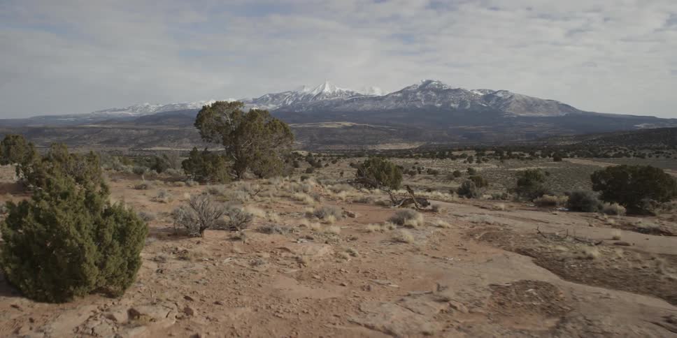 Aerial view passing two people sitting next to their tent in a barren wilderness and the view moving towards the distant mountains