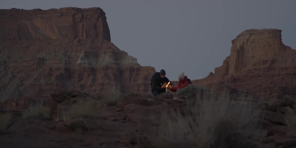 Two people lighting a fire on top of a mountain