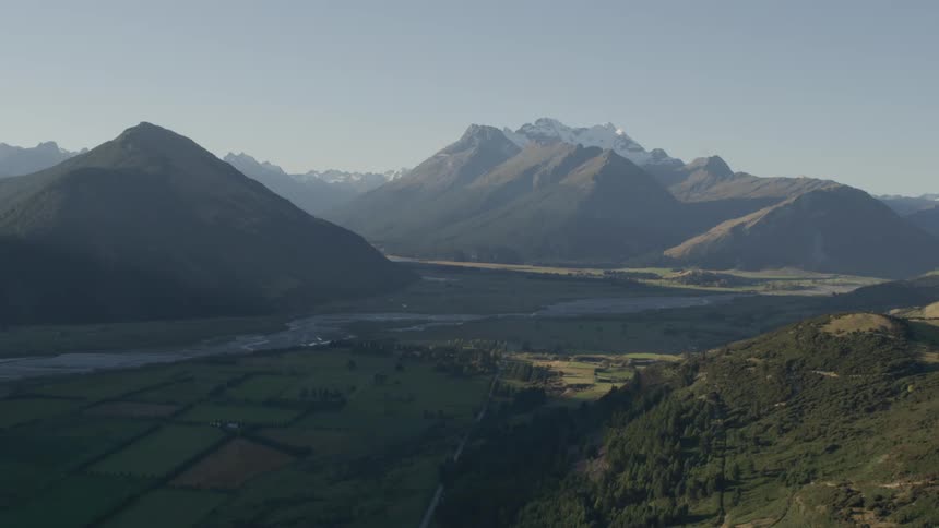 Farmland around a river in a mountain valley with patches of sunlight and shade