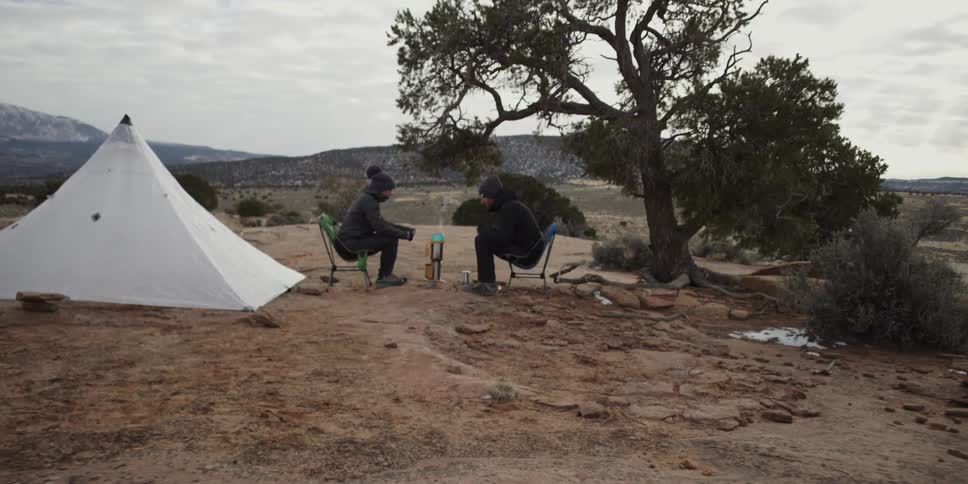 Two campers sit beside their tent heating coffee