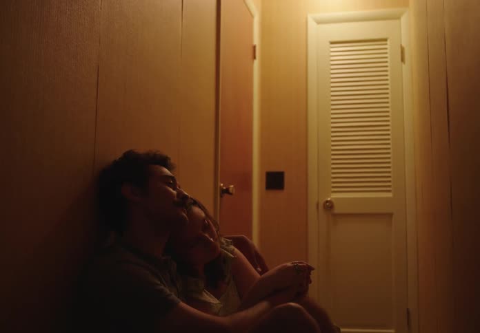 A couple sitting on the floor of a narrow corridor holding each other and looking sad