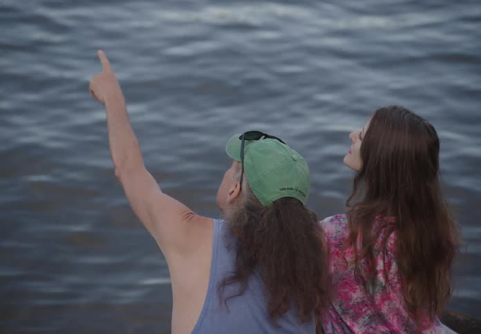Couple sitting by the sea with a man pointing his finger up