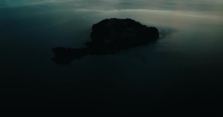 A solitary island emerges from calm waters during twilight