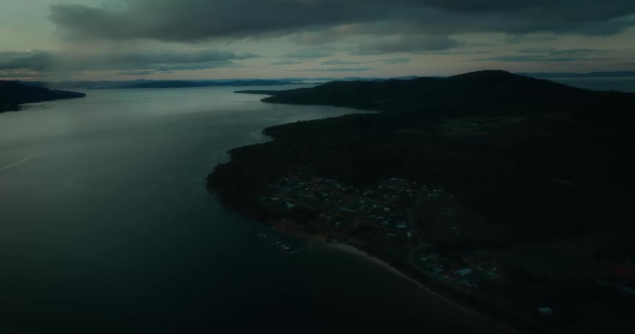 An aerial view of a serene coastline at dusk with a small town nestled along the shore and calm waters stretching into the distance
