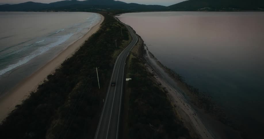 Aerial panorama of a vehicle traveling on a road surrounded by two beaches and mountains on the horizon