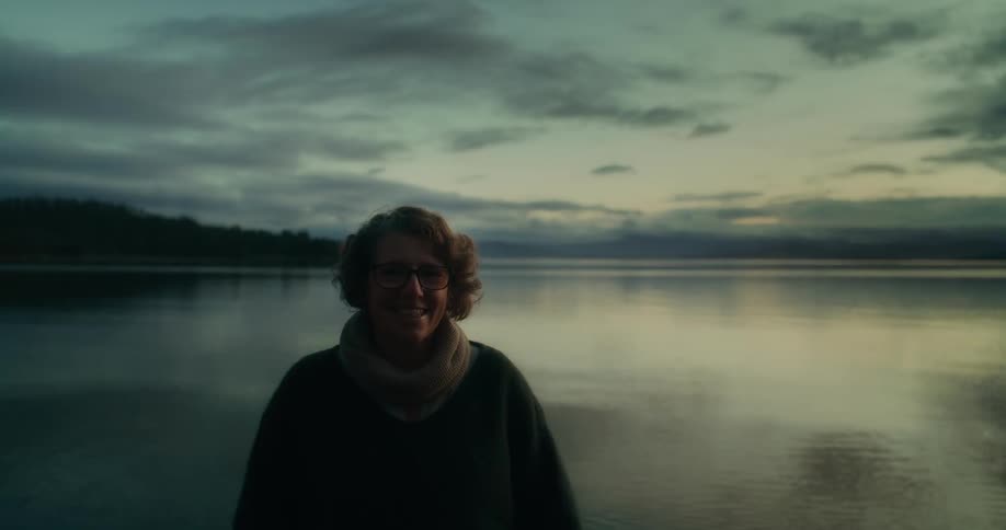 A middle aged woman in front of a large lake smiling