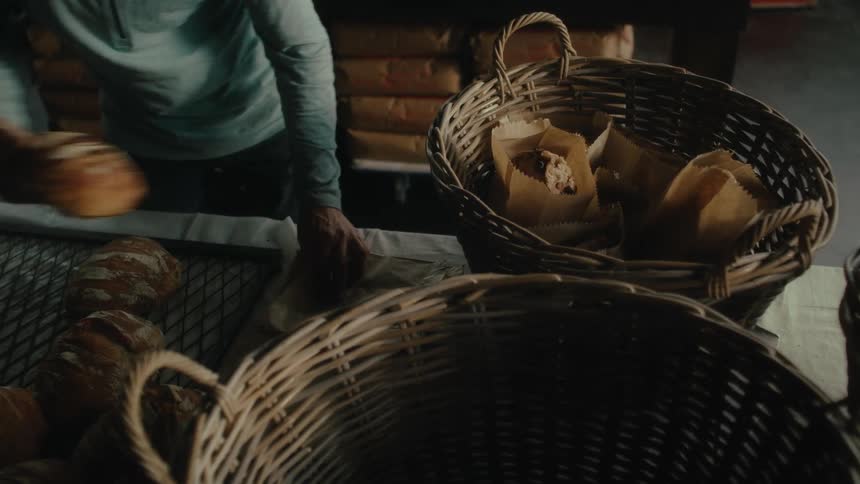 Close up of a person bagging freshly baked bread placing them on wicker baskets