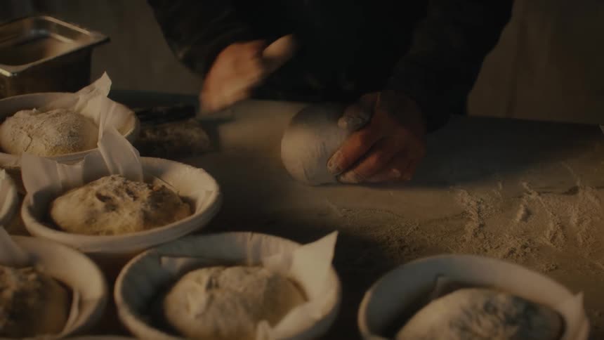 A persons hands kneading dough for bread round loaves of bread with flour dusting
