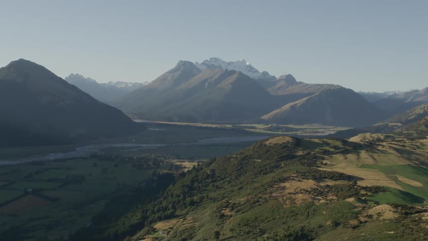 Aerial of a river valley that lies between a mountain range on a sunny day