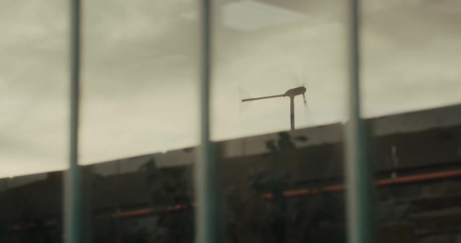 A wind turbine spinning over the rooftop of a building under a cloudy sky