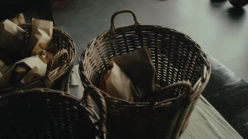 A person filling a wicker basket with bread loafs in bronw paper bags