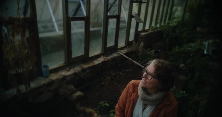 Woman sitting next to a greenhouse in a vegetable garden at night
