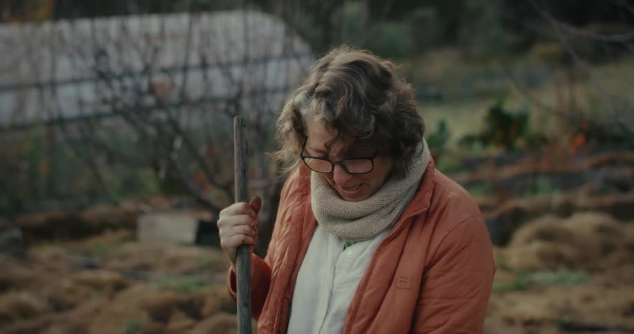 A woman looks over at someone who is smiling and talking while she rakes her lawn