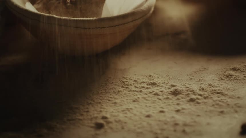 A closeup shot of flour being sifted into a bowl creating a soft dusty atmosphere