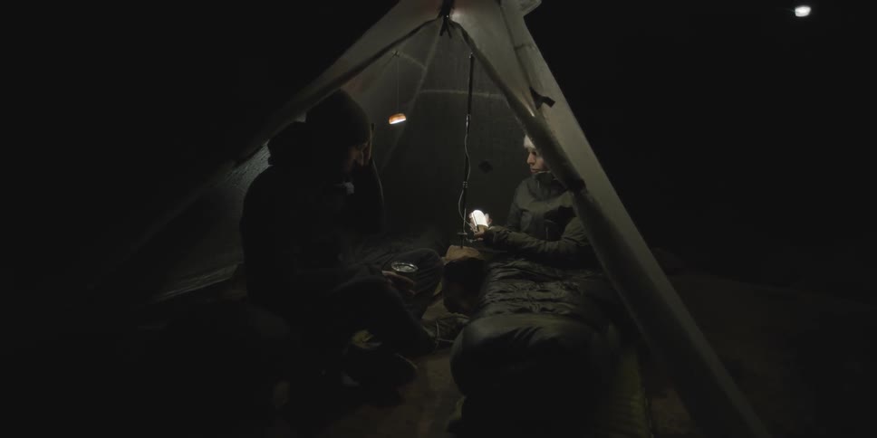 Two people sitting in their tent after dark