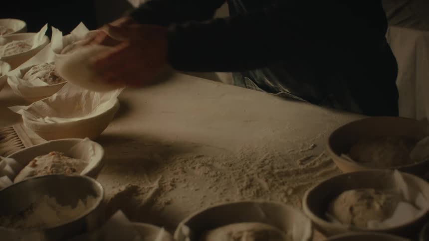 Pair of hands preparing bread dough on a table and placing it in a bowl