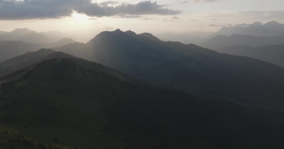 A mountainous landscape during sunrise or sunset with light rays piercing through the clouds onto the peaks