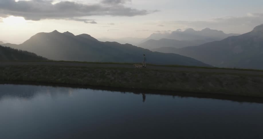 A woman walking a dog near a lake in the mountains at morning