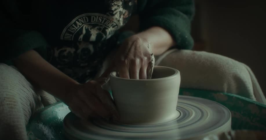 A persons hands shape a clay pot on a pottery wheel
