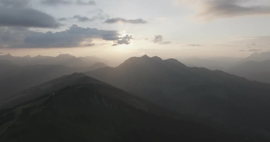 Fog covers the silhouette of a mountain peak with the sunlight on the horizon in the background
